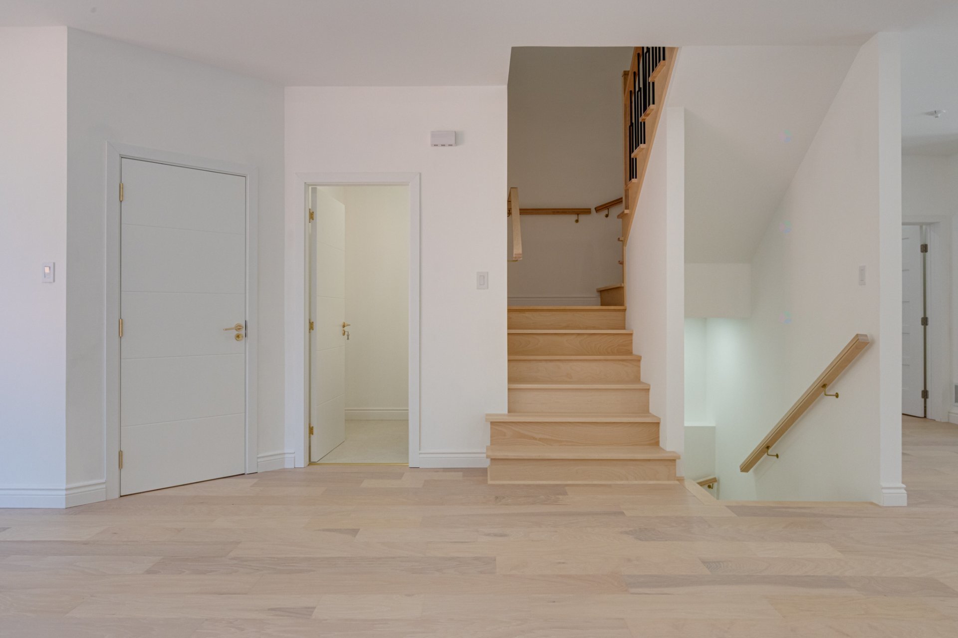 Bright white hallway with pale wood floors, doors, and a staircase leading both up and down.