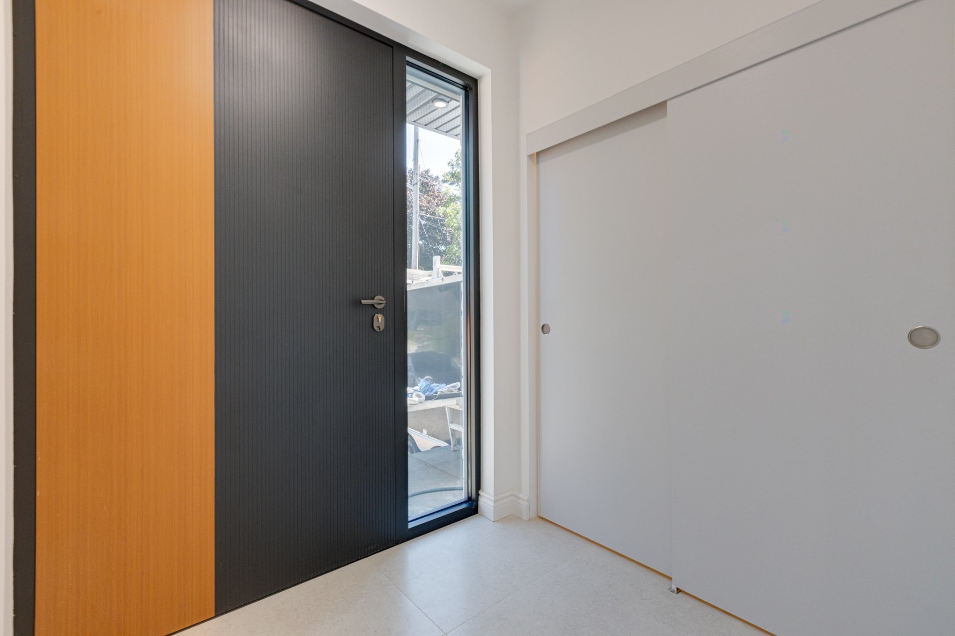 Modern entryway with a ribbed black door, glass sidelight, wood panel, and large white sliding panel.