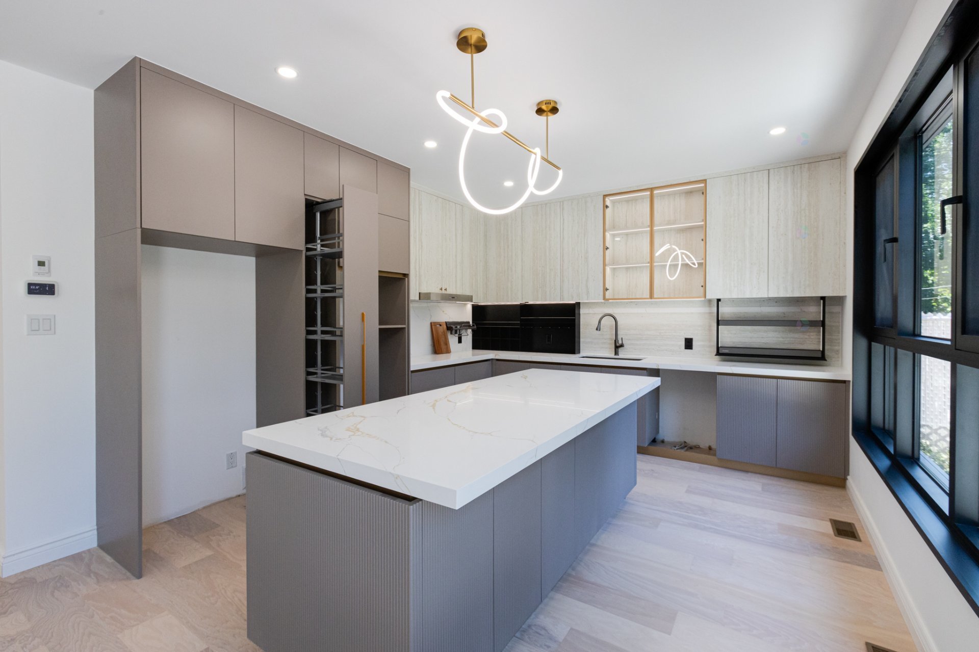 Modern gray-and-white kitchen with a marble island, ribbed cabinets, looping pendant lights, and large windows.